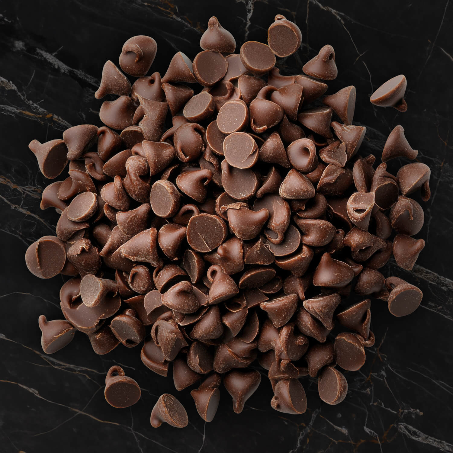 Gotas de chocolate amargo de alta qualidade amontoadas sobre uma superfície de mármore preto, representando a pureza do ingrediente utilizado na cobertura do Ptichye Moloko da Épacomê.